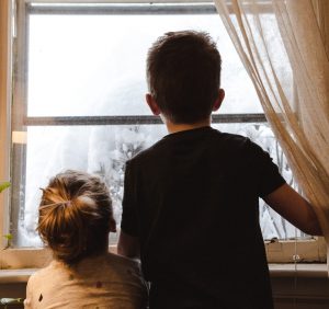 Two children looking through a window at snow